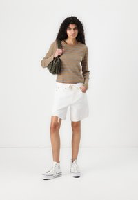 Haut à manches longues rayé marron et beige, short en denim blanc avec des bords effilochés, et baskets montantes blanches. Sac vert porté sur l'épaule.