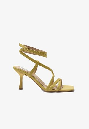 Sándal de tacón alto amarillo con tirantes, punta cuadrada y correa con hebilla en el tobillo, mostrado de lado sobre un fondo blanco.