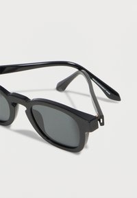 Gafas de sol rectangulares negras con lentes oscuras y el texto "VALORES DE SOSTENIBILIDAD ARMANI" en el interior de la patilla.