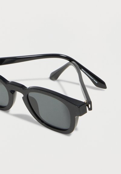 Μαύρα ορθογώνια γυαλιά ηλίου με σκούρους φακούς και το κείμενο "ARMANI SUSTAINABILITY VALUES" στο εσωτερικό του βραχίονα του πλαϊνού μέρους.