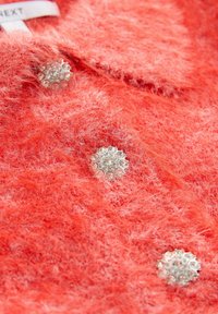 Koraļļu mīksto audumu ar trim apaļām pogām, kas rotātas ar caurspīdīgām rhinestones, sakārtotām vertikāli.