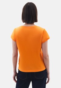 Oranžové tričko s krátkým rukávem a kulatým výstřihem, vyrobené z měkké tkaniny, s čistým zadním dílem a jednoduchými švy.