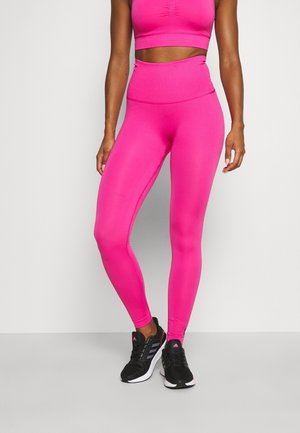 Lyserød sports-bh og højtaljede leggings, lavet af strækbart materiale med ribbet tekstur. Båret med sorte sportssko.