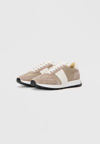 Semsket og lær sneakers i beige og krem med en hvit mellomsåle, flate snørebånd og en teksturert gummisåle. Minimalistisk design.