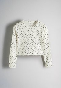 White ribbed long-sleeve cropped shirt with small brown flower pattern on a light gray background.