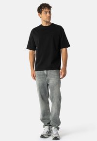 Czarny t-shirt z krótkim rękawem i okrągłym dekoltem, noszony z jasnoszarymi dżinsami i szaro-srebrnymi sneakersami z zielonymi akcentami.