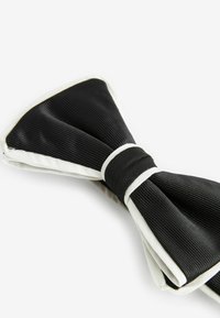 Schwarze Seidenfliege mit plissierter Textur und weißem Besatz. Verfügt über ein zentrales Band aus Stoff, das die Schleife befestigt und ein klassisches Design präsentiert.