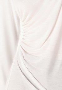 Light pink top with a soft, textured fabric, featuring gathered detailing on the side for a draped effect.