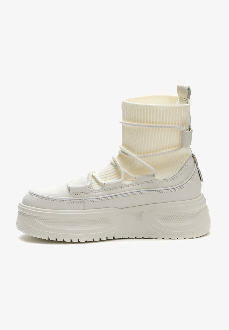 Valkoiset tennarit, joissa on pehmeä päällinen, ribattu sukka, ja muhkea pohja, jossa on tekstuuripintoja ja elastisia yksityiskohtia.