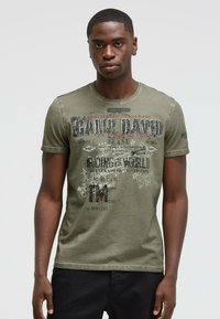 Green cotton t-shirt featuring a round neckline and short sleeves. Design includes printed graphics and text in contrasting colors.