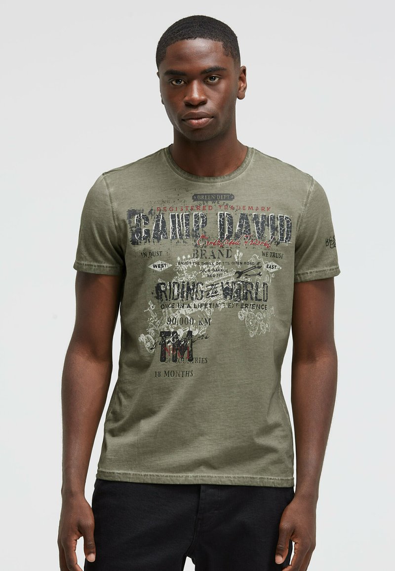 Green cotton t-shirt featuring a round neckline and short sleeves. Design includes printed graphics and text in contrasting colors.