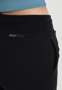 Pantaloni da jogging neri realizzati in tessuto morbido, con vita elastica, tasche laterali e un logo stampato vicino alla vita.