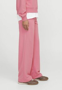 Roza široke trenirke iz mehkega materiala, z visokim pasom in ohlapnim krojem, v kombinaciji s svetlo rjavimi športnimi copati.