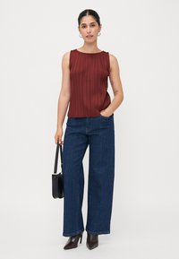 Débardeur plissé bordeaux avec un col rond, associé à un jean large bleu foncé. La tenue comprend des talons aiguilles marron et un sac à main noir.