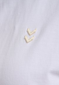 White fabric with two small embroidered chevron shapes in off-white thread, arranged vertically.
