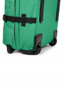 Grön väskan av tyg med svarta detaljer, med en texturerad yta, dragkedjor och dubbla snurrande hjul för enkel rörlighet.
