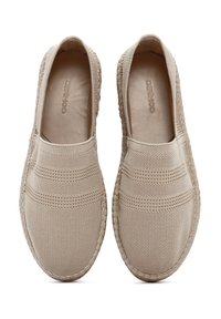 Scarpe beige senza lacci con tomaia in rete testurizzata, cuciture decorative e suola intrecciata. L'interno presenta un rivestimento morbido per il comfort.