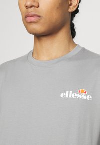 Gray cotton t-shirt with a crew neck and short sleeves, featuring a white "ellesse" logo with a colorful accent above it.