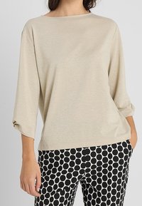 Beige, lehký top s dlouhým rukávem a širším výstřihem. V kombinaci s kalhotami s černobílým puntíkovaným vzorem, které mají volný střih a rolled sleeves.