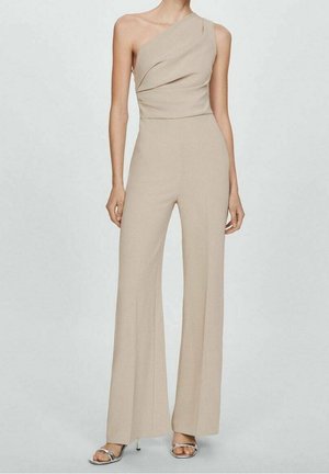 Beżowy kombinezon na jedno ramię z drapowanym stanikiem, prostymi nogawkami i gładką fakturą. Połączony z srebrnymi sandałami na wysokim obcasie.