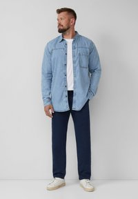 Lichtblauwe denim overhemd met een knoopsluiting, borstzak en donkerblauwe broek. Het schoeisel is wit met een gemêleerde zool.