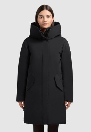 Geacă căptușită neagră, cu guler înalt, închidere cu fermoar, buzunare laterale și mâneci lungi. Textură netedă și design simplu.