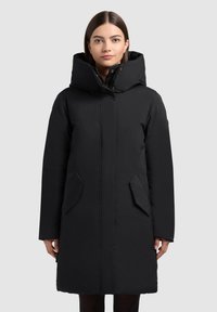 Černý prošívaný kabát s vysokým límcem, zapínáním na zip, bočními kapsami a dlouhými rukávy. Hladká textura a jednoduchý design.
