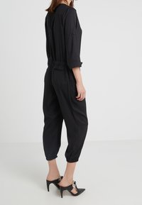 Une combinaison noire avec une coupe décontractée, des manches trois-quarts, une taille élastique et des jambes raccourcies. Associée à des chaussures à talons hauts noires.