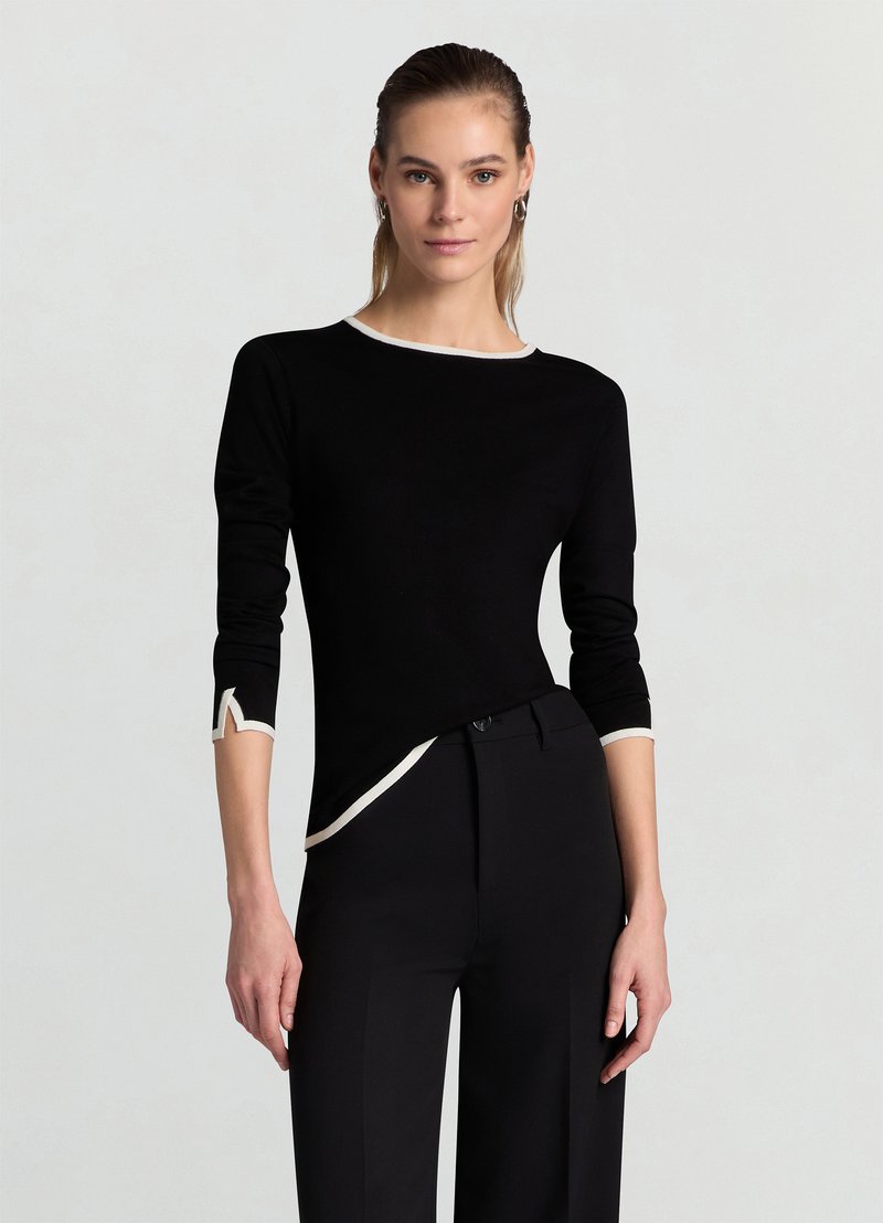 Schwarzes Langarmshirt mit weißer Paspelierung, rundem Ausschnitt und einzigartigen, eckigen Details an den Ärmeln. Weicher Stoff mit figurbetontem Schnitt.