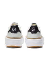 Weiße Ledersneaker mit einem schwarzen Fersenakzent, einer dicken weißen Sohle und auffälligem "Cole Haan"-Markenlogo auf der Rückseite.