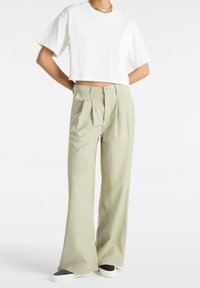 Avskuren vit bomullströja kombinerad med ljusgröna veckade vida byxor, med knappstängning och en avslappnad passform.