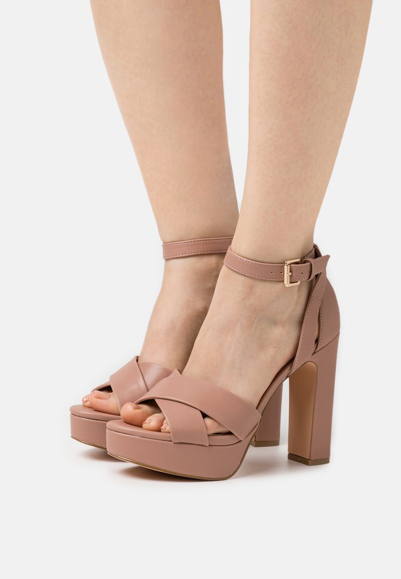 Sandales à plateforme en simili cuir rose avec des brides croisées à l'avant, une bride à la cheville et un talon épais. Texture lisse et design ouvert.