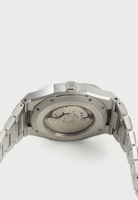 Montre en acier inoxydable avec une finition brossée, boîtier octogonal, fond transparent, détails du mouvement automatique et un bracelet à maillons.