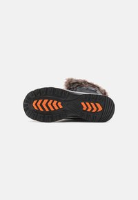 Botte noire avec une semelle en caoutchouc texturée présentant des accents oranges, un revers en fourrure douce, et un design robuste adapté à une utilisation en extérieur.