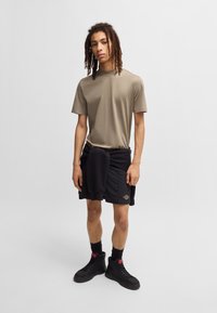 Maglietta a maniche corte verde oliva abbinata a pantaloni corti neri. Calze e scarpe alte nere con accenti rossi. Tessuto testurizzato e vestibilità comoda.