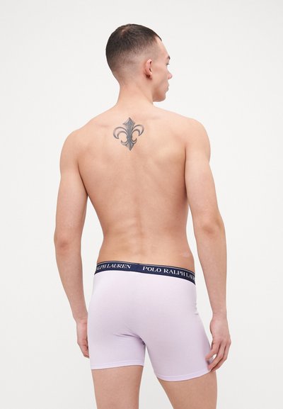 Fialové boxerky s námorníckym elastickým pásom s nápisom "POLO RALPH LAUREN." Zobrazené zozadu, odhaľujúce tetovanie.
