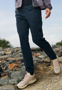 Marine atletiske bukser med elastisk linning, med en glatt tekstur. Kombinert med lyse sneakers med mesh-detaljer og snøring.