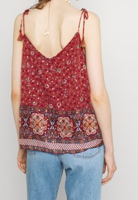 Top senza maniche rosso con fiori, dotato di scollo a V, spalline regolabili con laccio e orlo decorativo ricamato con motivi e trame intricate.