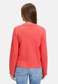 Sweatshirt corail avec un col, manches longues et tissu texturé, associé à un jean bleu clair. Présente une coupe décontractée et un design simple.