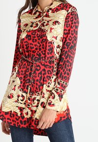Rød og sort leopardprint skjorte med guld kæde detaljer, lange ærmer, knaplukning og bælte i taljen. Fremstillet af glat stof.