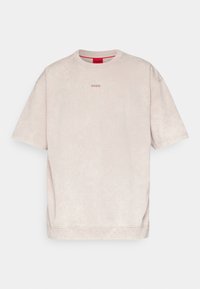 T-shirt beige clair à manches courtes avec petit logo "HUGO" centré en marron clair, col rond et tissu légèrement texturé.