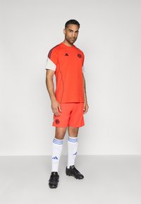 Piros sportmez fehér ujjakra, fekete díszítéssel, azonos piros sorttal, fehér zoknikkal kék csíkokkal, és fekete focicipővel.