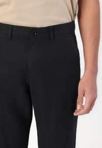 Pantalones de lino negros con un corte recto, que presentan un cierre frontal con botón y pasadores para cinturón. Textura suave con detalles de costura mínimos.