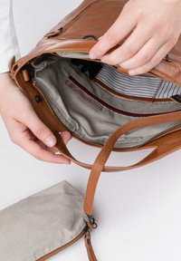 Bruine leren tas met een gestreepte stoffen voering. Voorzien van een rits bovenkant en een kleine bijpassende gestreepte pouch die is bevestigd.