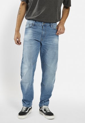 Blugi din denim bleu deschis cu o croială confortabilă, spălați ușor, cu detalii subtile de cusătură. Asortați cu adidași negri și albi.