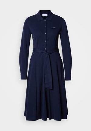 Vestido de algodão azul-marinho com gola, fecho de botão frontal, mangas longas e cinto na cintura para definir a silhueta; apresenta detalhe do logotipo.