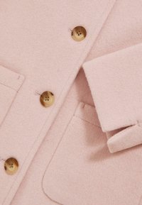 Abrigo de mezcla de lana rosa con botones de tono dorado, que presenta dos bolsillos frontales y un cuello con muesca, mostrando una tela suave y texturizada.