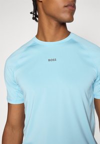 Lysblå træningsshirt med korte ærmer, lavet af glat materiale. Har et lille gråt "BOSS" logo på brystet.