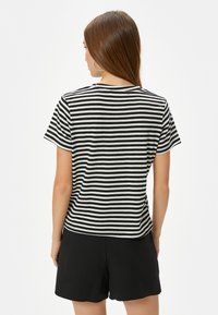 Camiseta de manga corta a rayas blanca y negra con cuello redondo, fabricada en un tejido suave y de corte holgado, combinada con pantalones cortos negros.