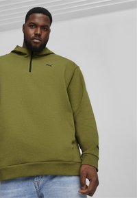 Oliven grøn hættetrøje med høj krave, kvart lynlås, struktureret stof og PUMA-logo i sort på brystet. Casual pasform med ribbede manchetter.